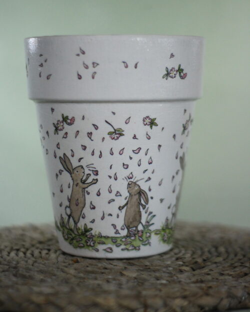 Plant pot with rabbit design on it, dancing in petals