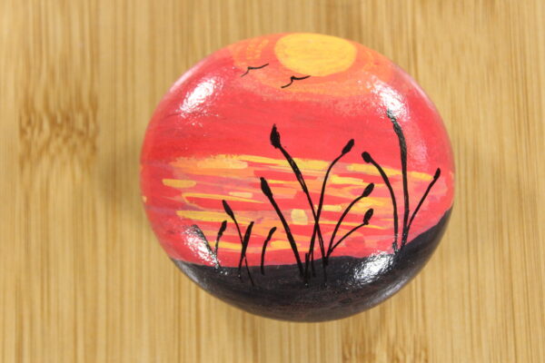 red sunset with reeds painted pebble